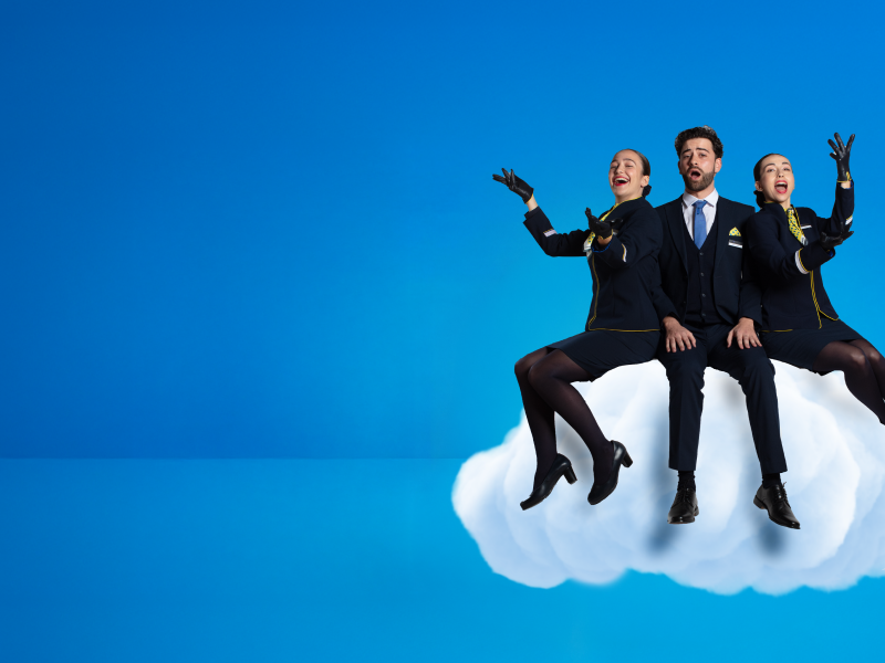 A group of cabin crew members: two woman and one man, who are sitting on a cloud looking forward and possing