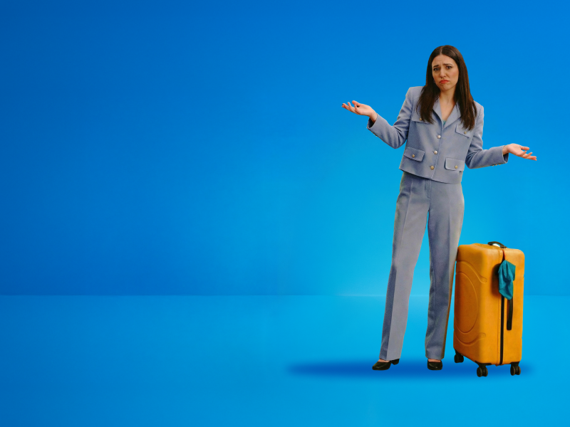 A woman beside her suitcase looking forward shrugging her shoulders and doubtful expression